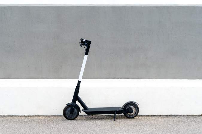A black and white e-scooter parked by the wall. How to charge e-scooter battery rightly?